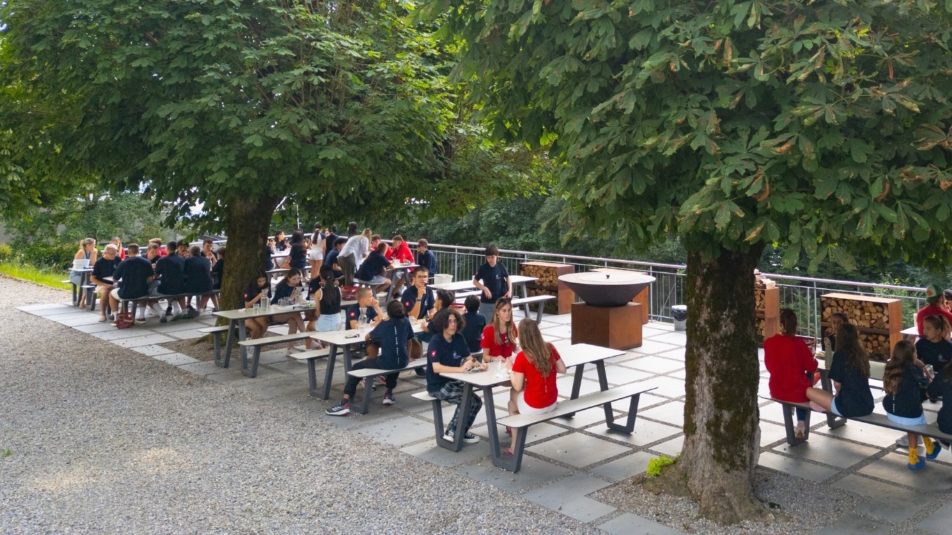 Eine Gruppe von Schülern genießt ihre Mahlzeiten in einem von Bäumen umgebenen Essbereich im Freien.