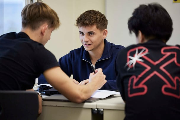 Drei männliche Schüler sitzen in einer Klasse und diskutieren über etwas.