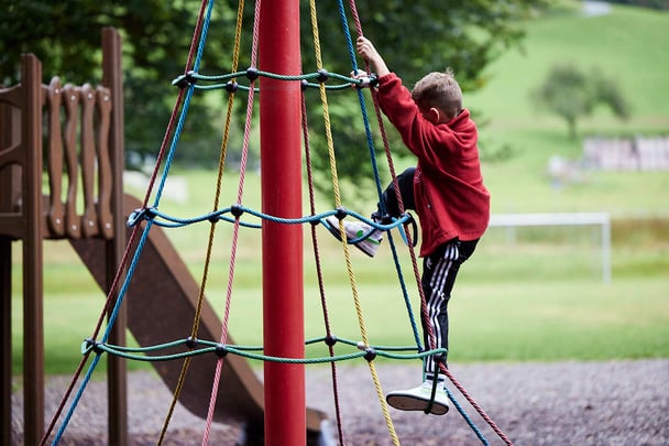 Ein junger Schüler klettert auf einem Seil und spielt auf einem Feld.