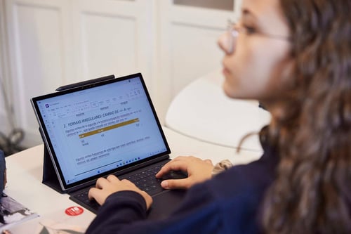 Eine Studentin auf einem Stuhl, mit einem Laptop vor sich, schaut in eine andere Richtung.