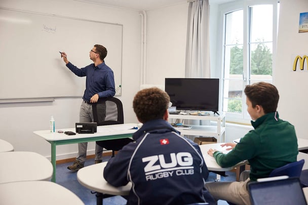 Ein männlicher Lehrer schreibt etwas an eine weiße Tafel und zwei Schüler passen auf.