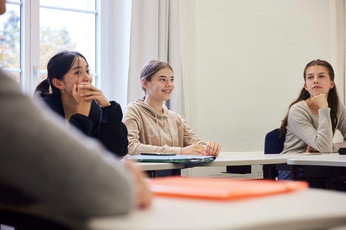 Drei Schülerinnen setzen sich in eine Klasse, jede mit einem anderen Gesichtsausdruck.