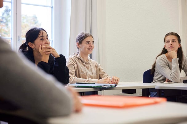 Drei Schülerinnen setzen sich in eine Klasse, jede mit einem anderen Gesichtsausdruck.