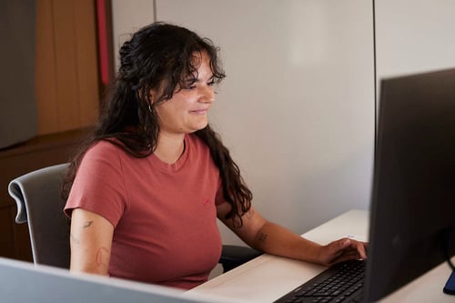 A female staff in brown top look at computer with smile.