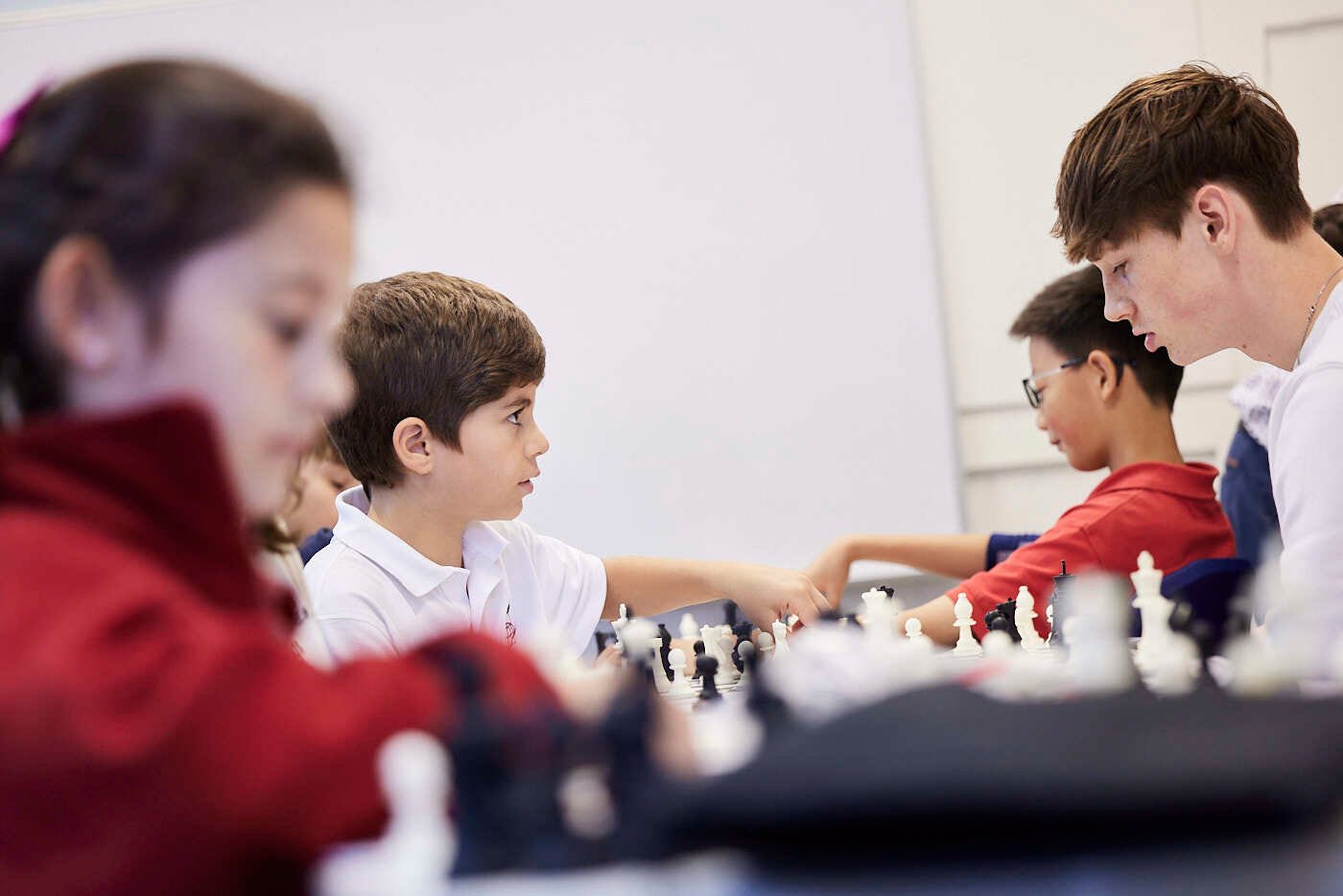 Mehrere junge Schüler und ein männlicher Mentor spielen Schach.
