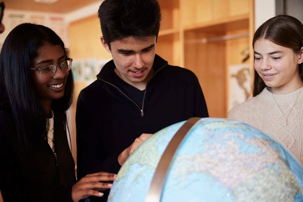 Zwei Schülerinnen und ein Schüler betrachten und lernen etwas über einen Globus