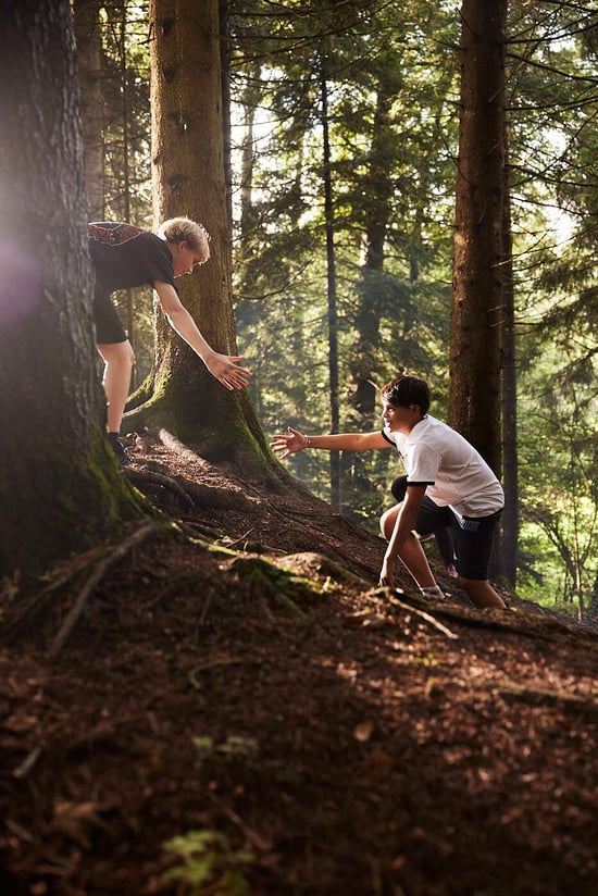Ein Schüler streckt seine Hand aus, um einem anderen Schüler in einem Wald zu helfen.