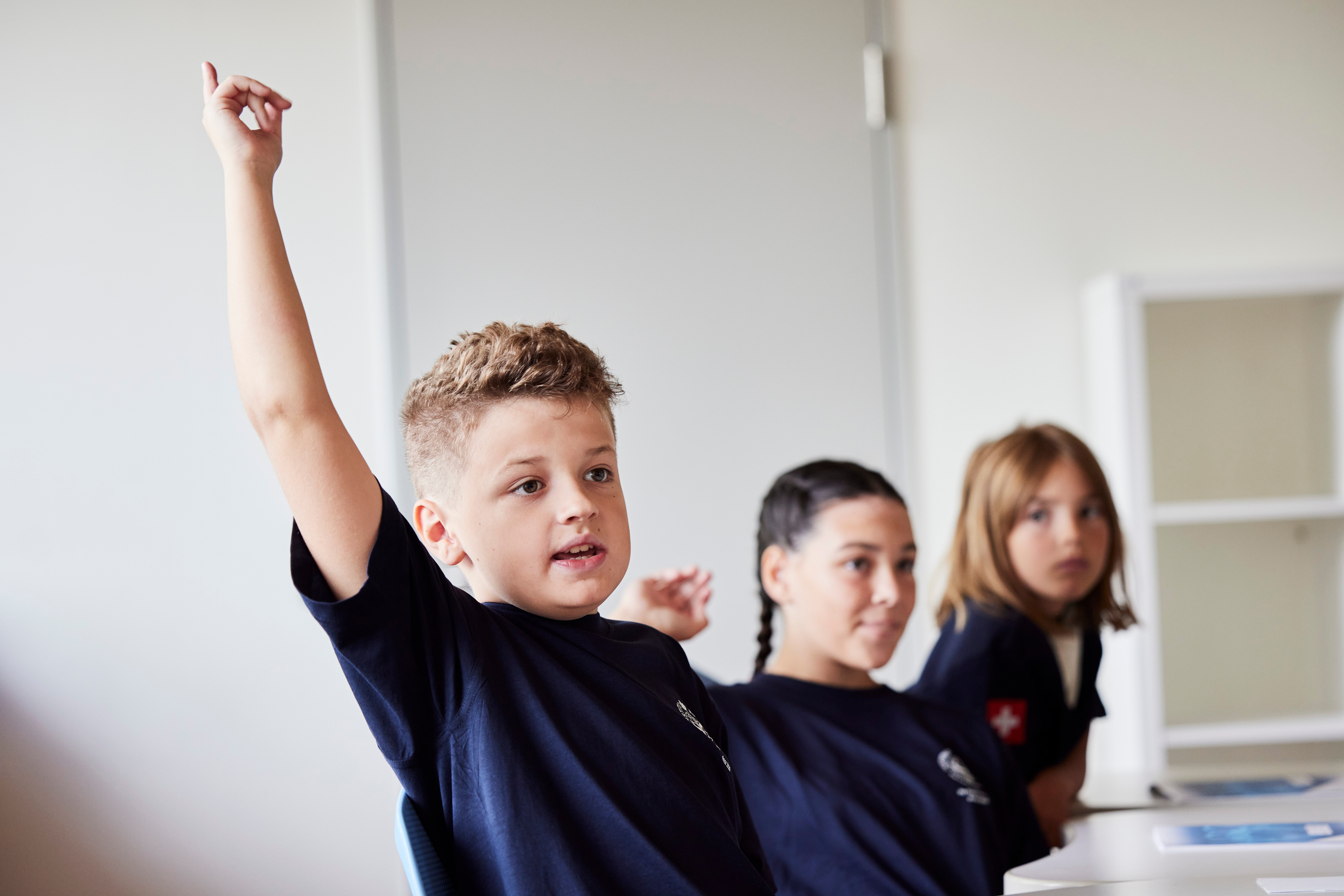 A boy sit with two other girl students in a class.
