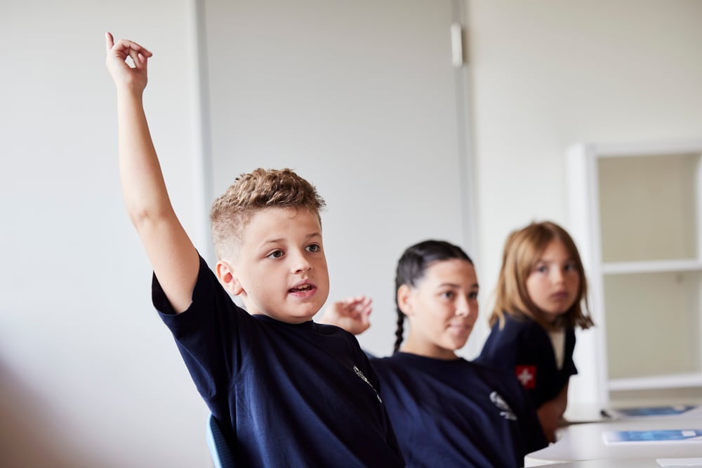 A boy sit with two other girl students in a class.