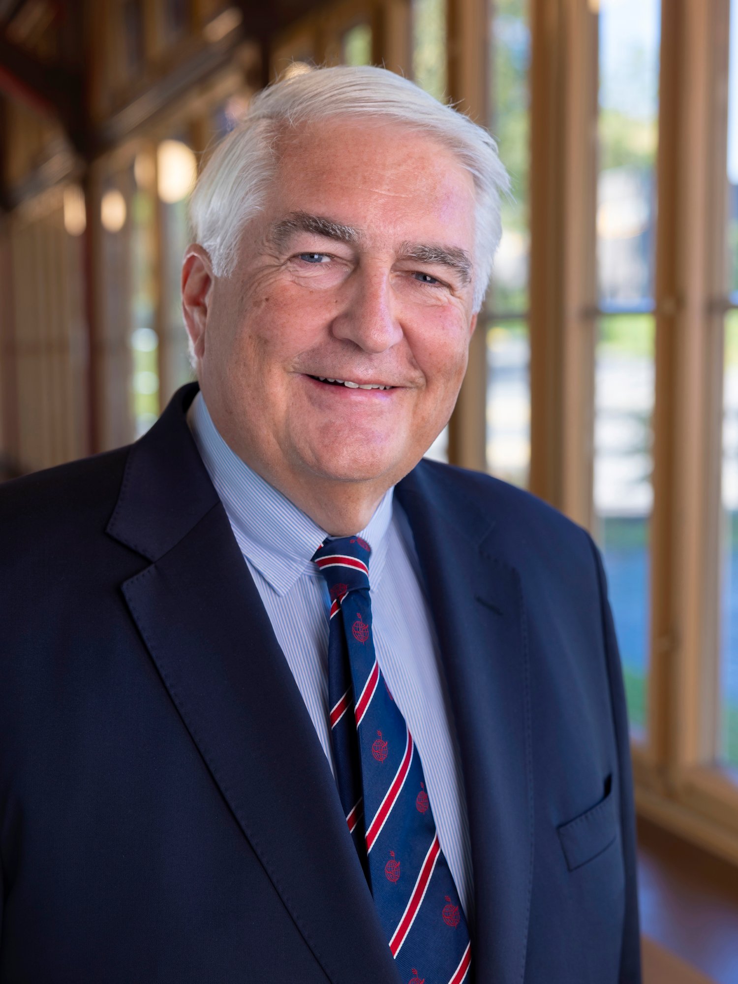 A senior man in suit in a corridor smiles at camera.