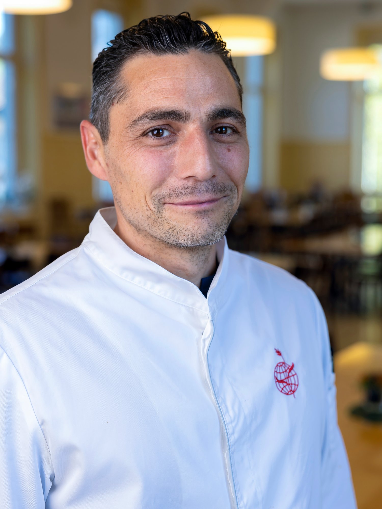 Close-up of a male cook wearing white top., smiling to camera.