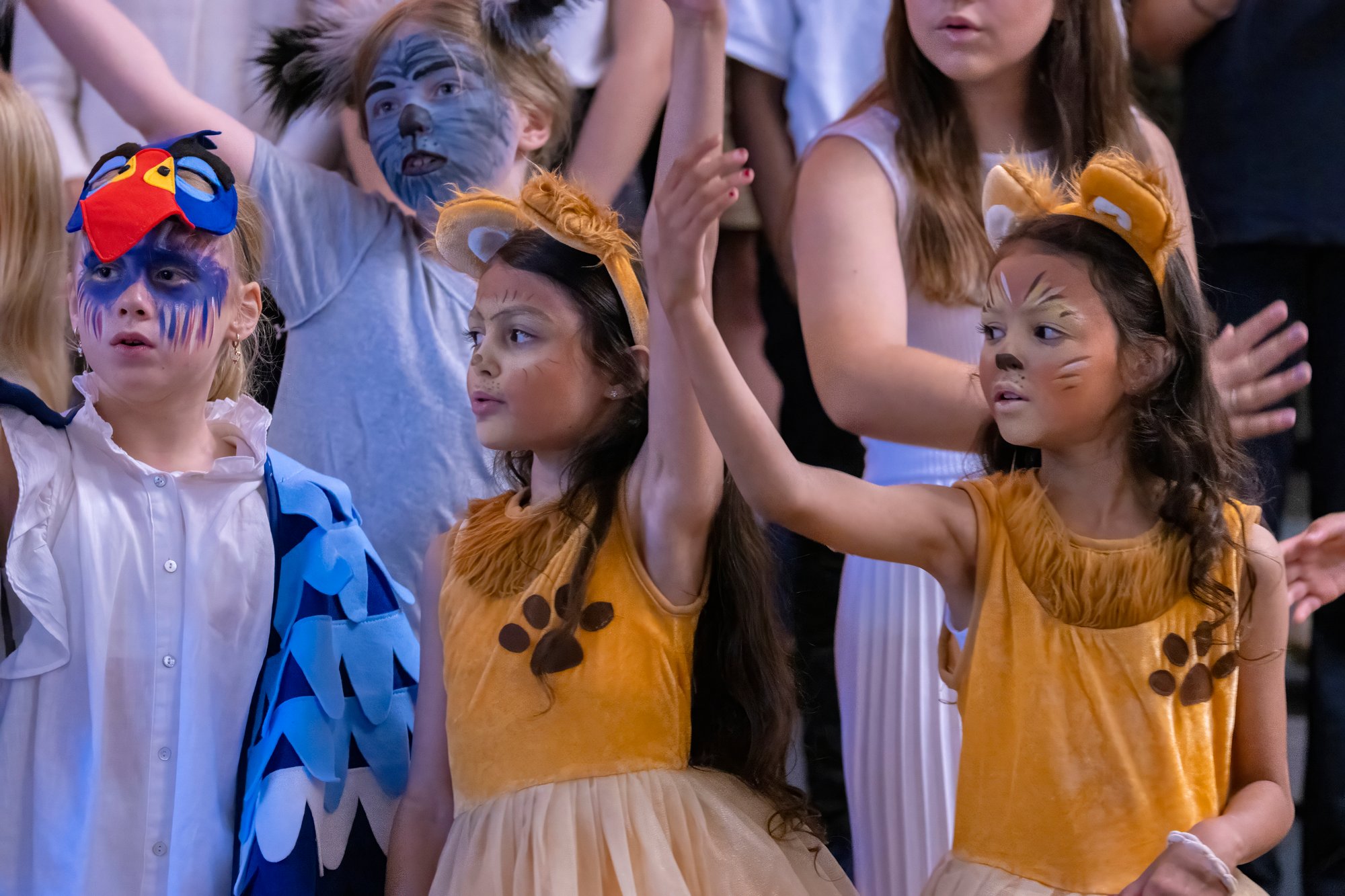 Eine Gruppe von Kindern führt ein Theaterstück auf, bei dem drei Mädchen im Vordergrund stehen.