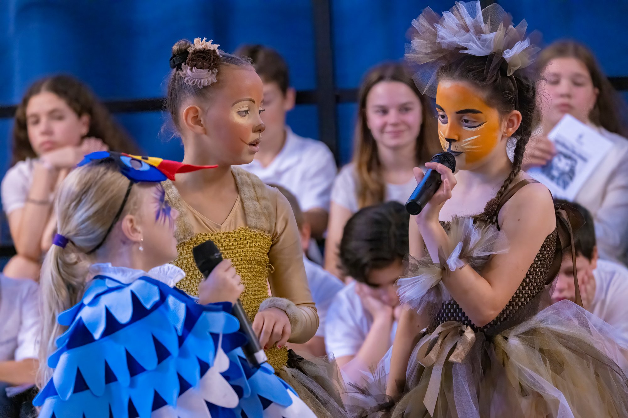 Eine Gruppe Kinder in verschiedenen bunten Kostümen führt ein Theaterstück auf.