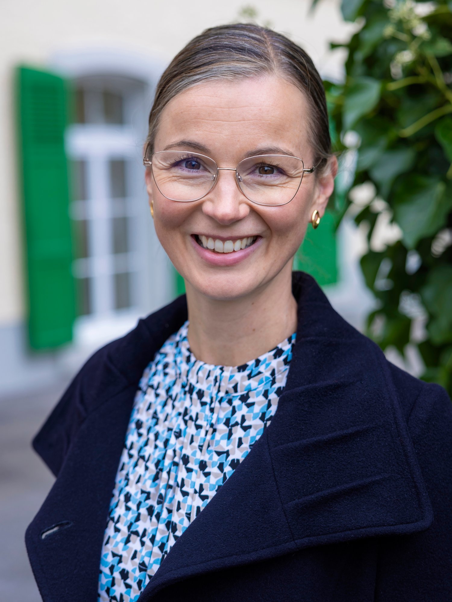 A female staff in black blazer and eyeglasses smiling at the camera.