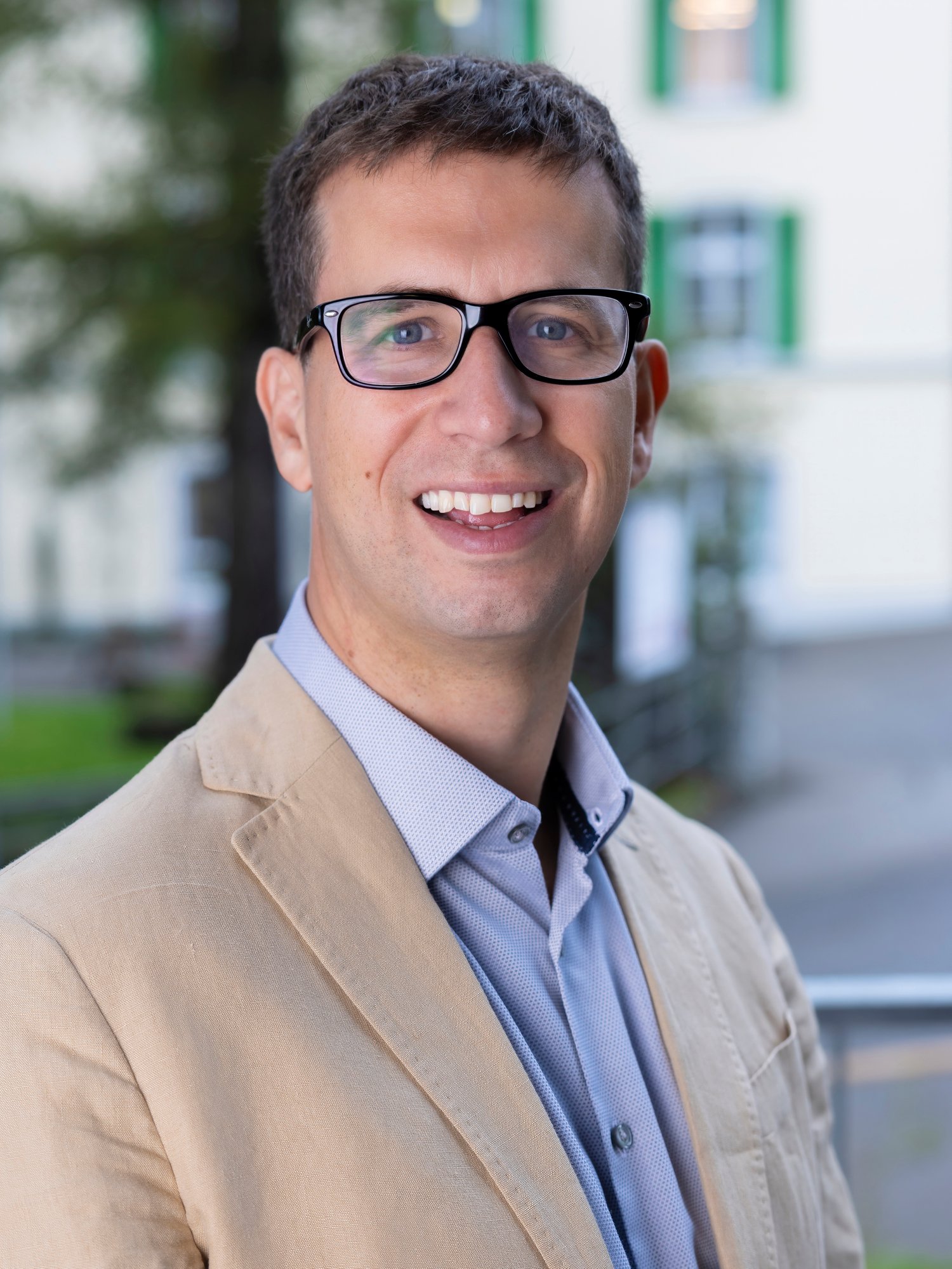 A male staff in suit and glasses look straight and smile to camera.
