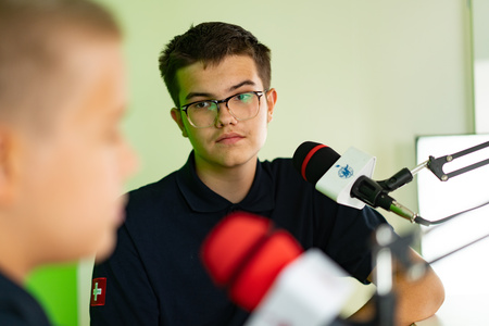 A boy student in a studio setting room interacts with another boy.