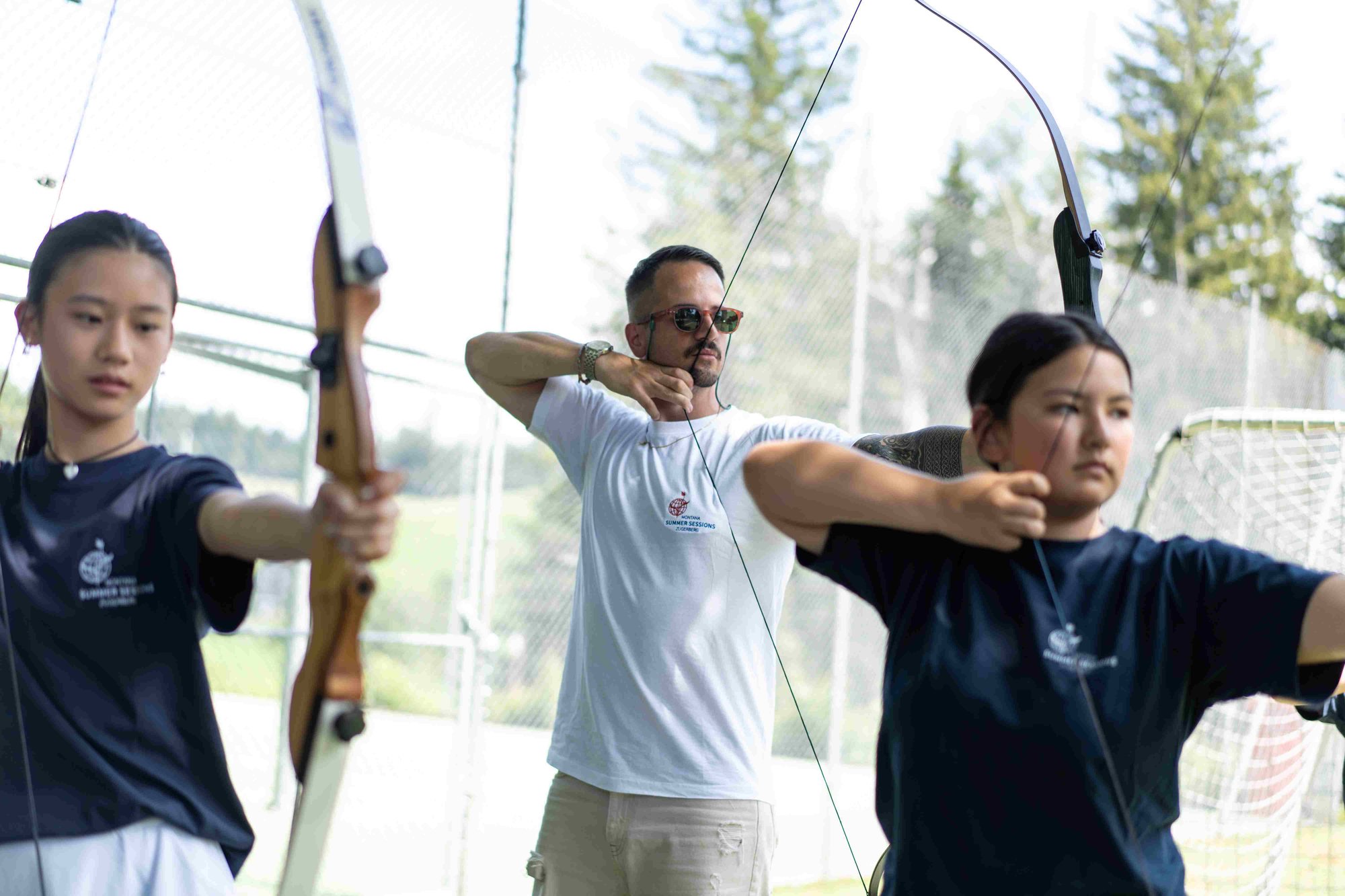 A teacher and two female students play archery.