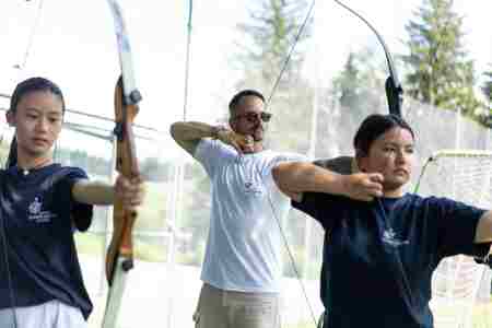 A teacher and two female students play archery.