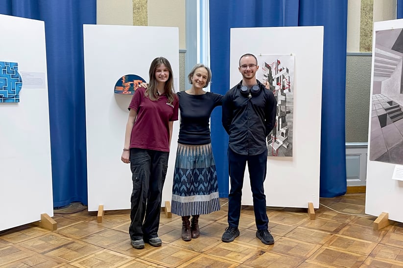 A middle-aged lady between a young lady and a young man in an exibition.