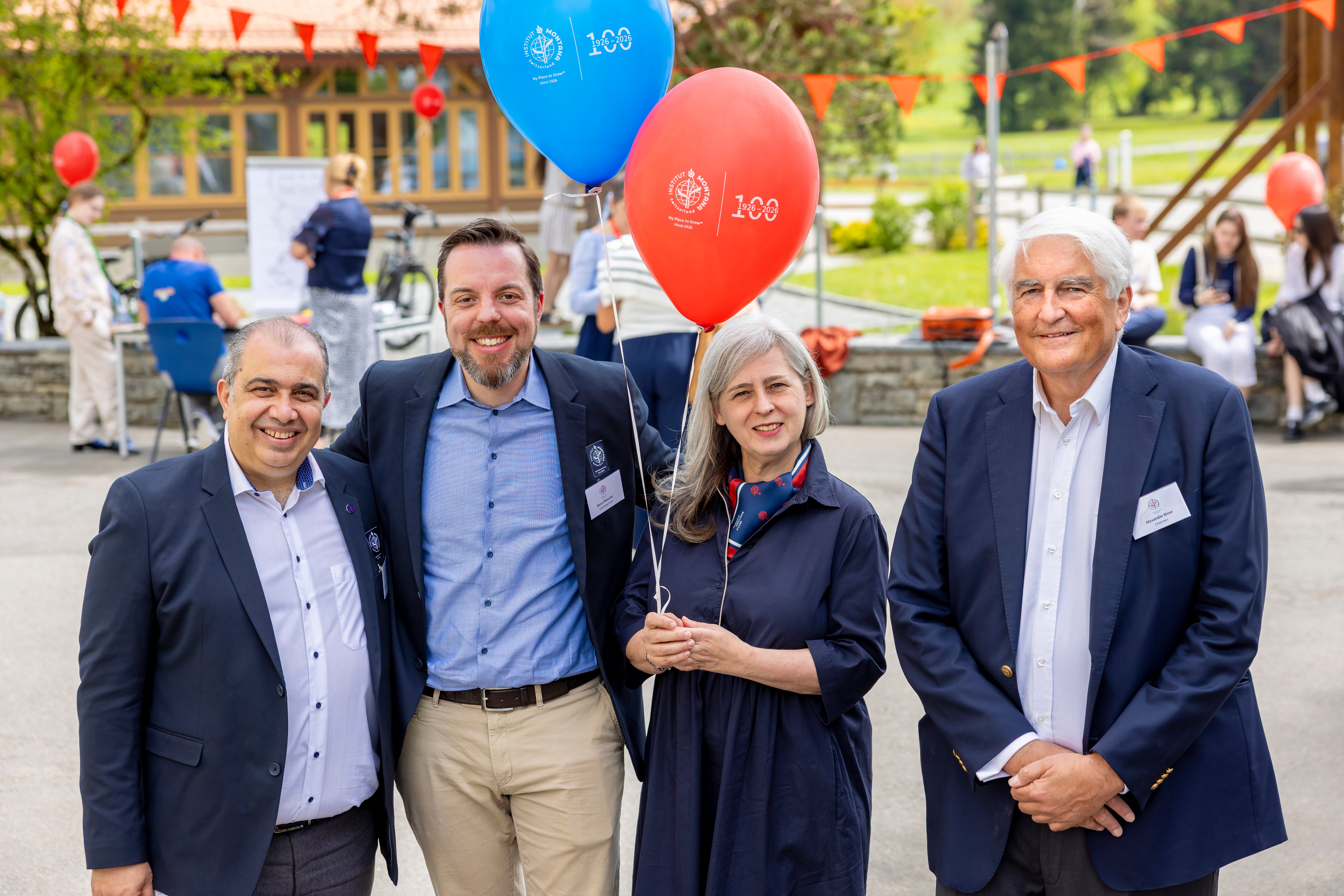 Four people stand and smile with balloons.