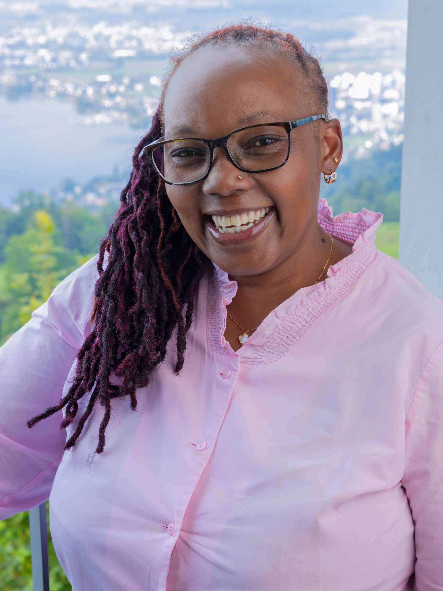 A female staff with glasses and pink top smiles at camera.