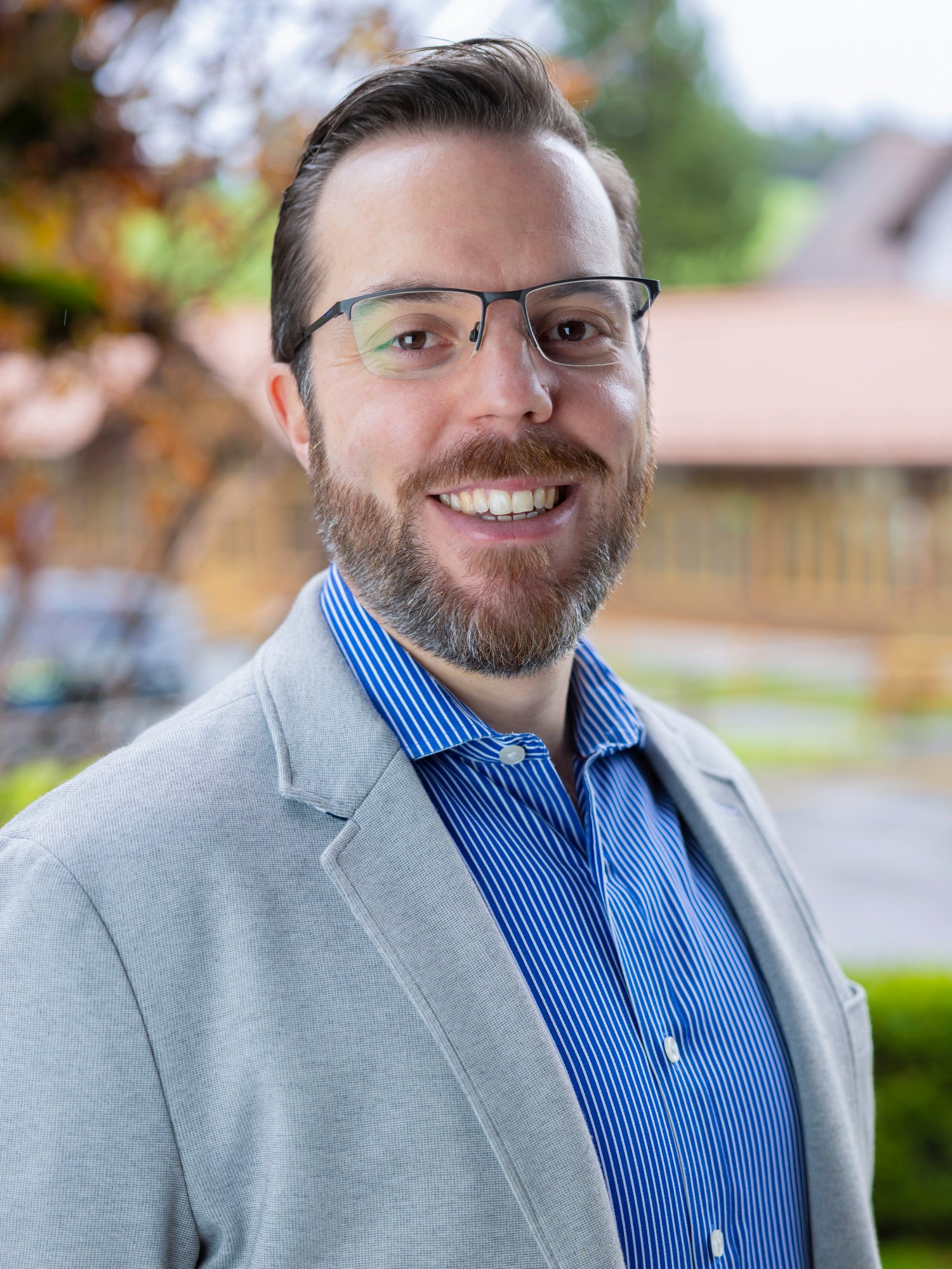 A male staff in grey suit and glasses smile to the camera.