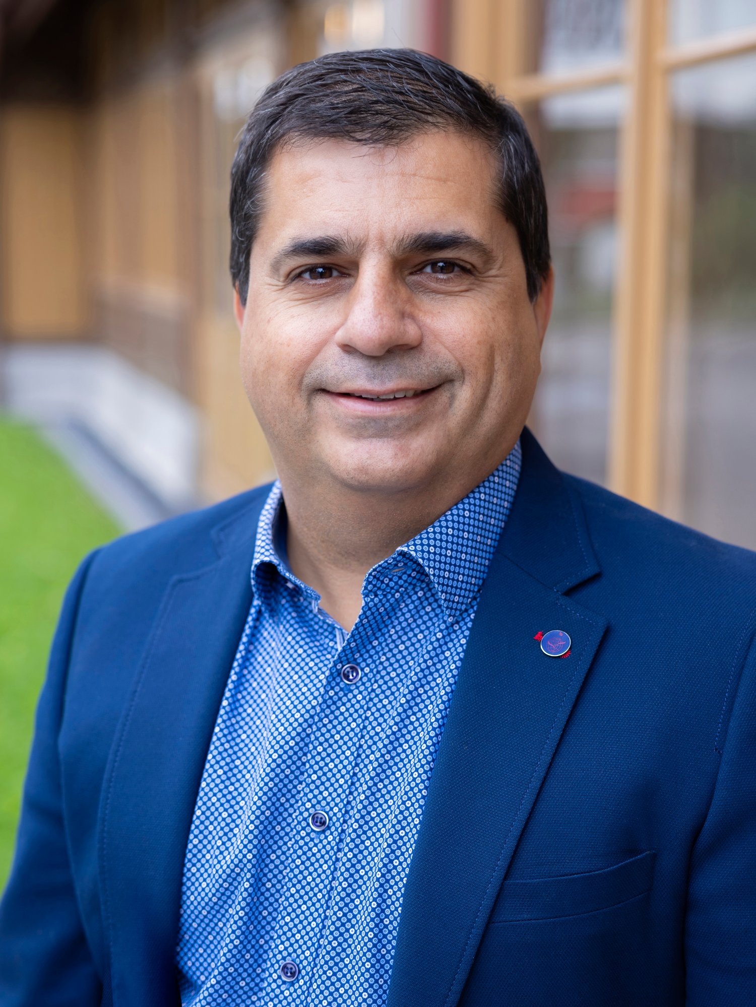 A male staff in blue blazer looking at camera, smiling.