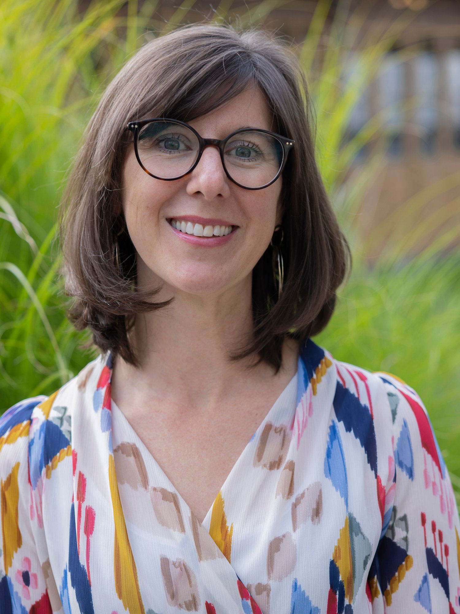 A female staff wearing colourful top and eyeglasses smiling.