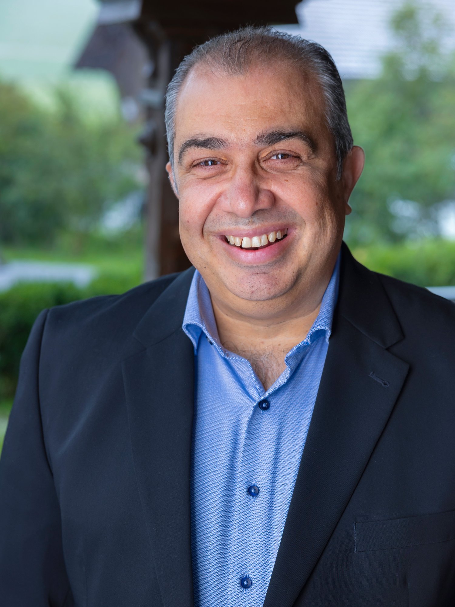 A male staff in dark grey suit smile to the camera.