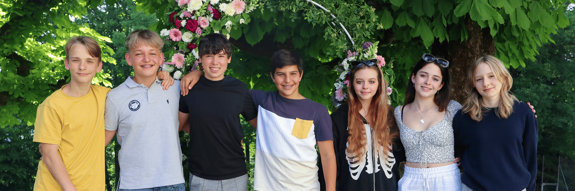 Sieben junge Schülerinnen und Schüler posieren in einem üppigen Garten.