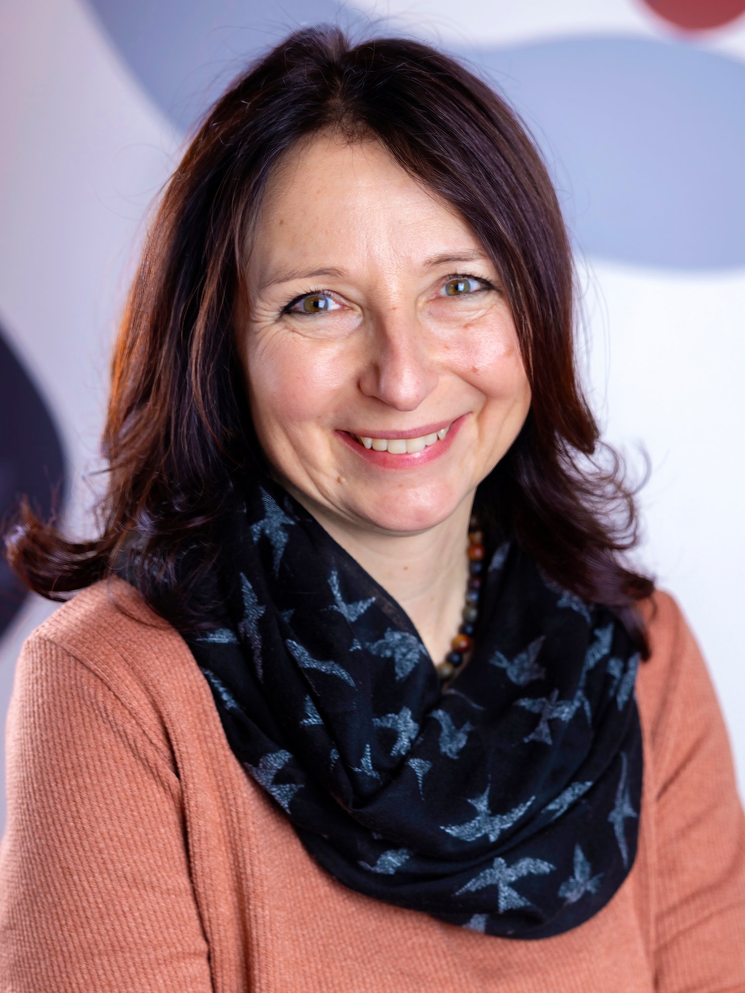 Eine Frau in einem braunen Oberteil lächelt in die Kamera.