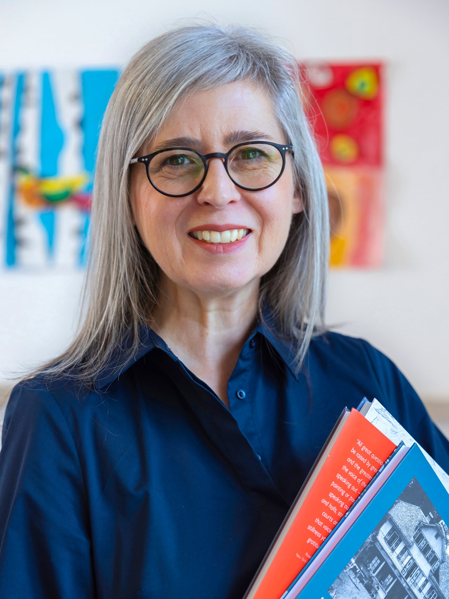A female staff in blue dress and glasses smile to camera.